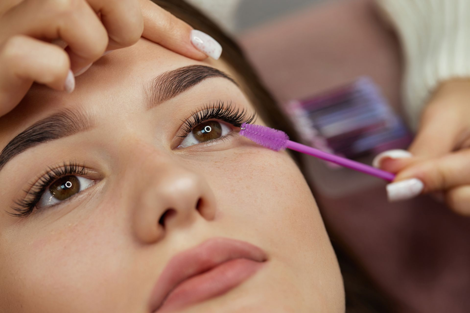 Close-up of a person having purple mascara applied to one eye with a brush.