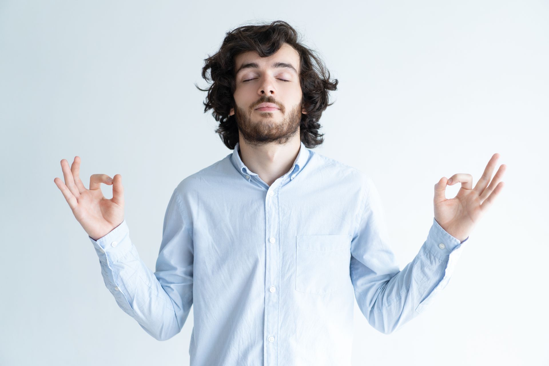 Person meditating with eyes closed against a light background, hands raised in a calm pose