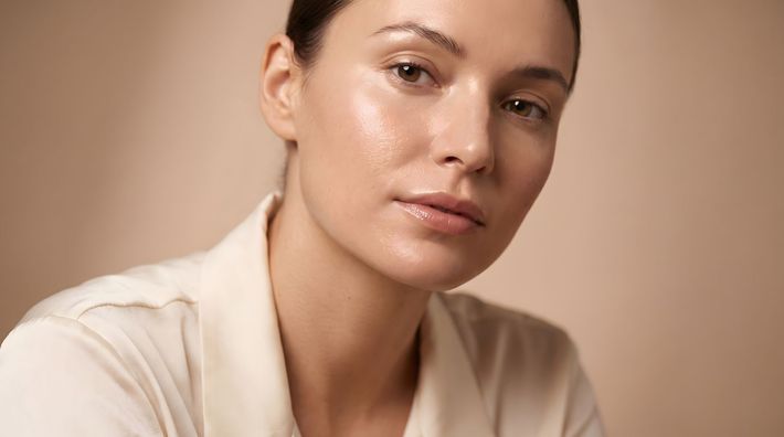 Portrait of a person in a cream top against a beige background, looking at the camera with a calm expression