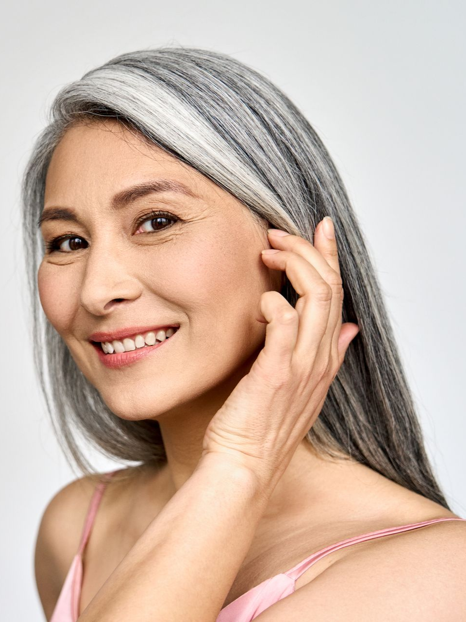 Smiling woman with long silver hair touching her ear against a white background