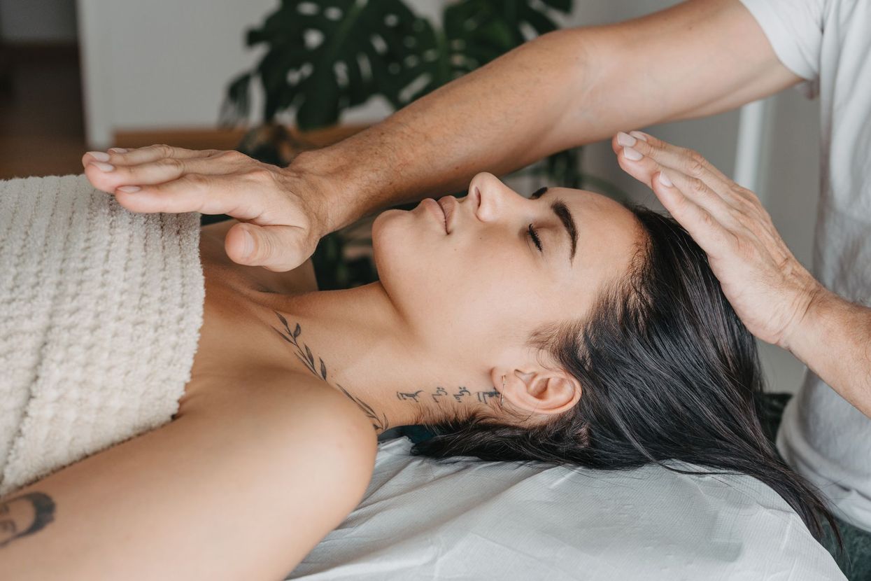 Person receiving a forehead hand massage on a spa bed, covered with a beige towel.