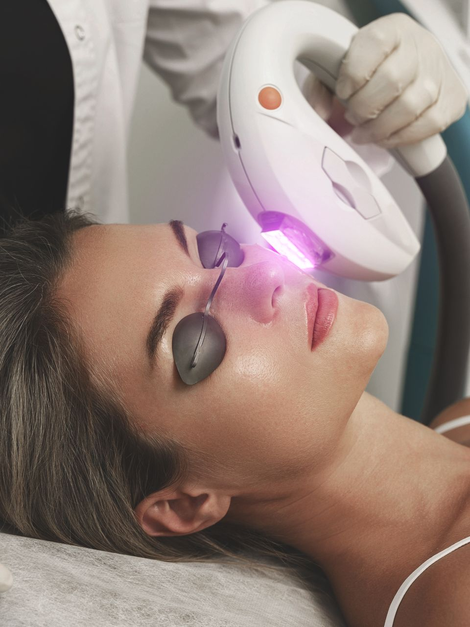 Woman receiving a pink facial treatment with a handheld device while lying on a spa bed