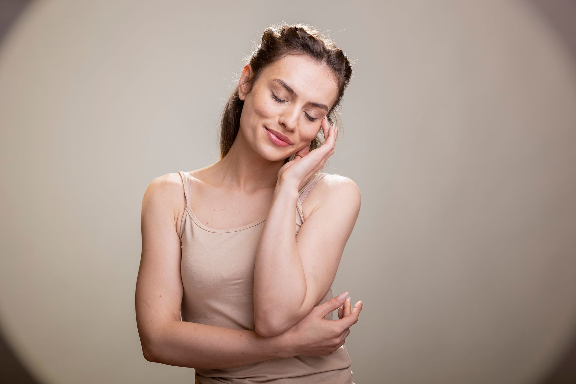 Woman in beige top resting her head on her hand against a neutral background