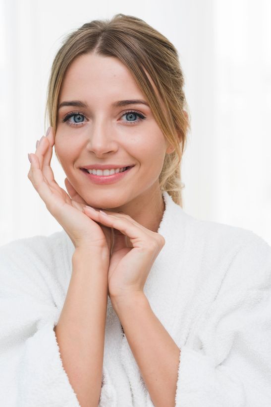 Smiling woman in white robe resting her face on her hands against a light background