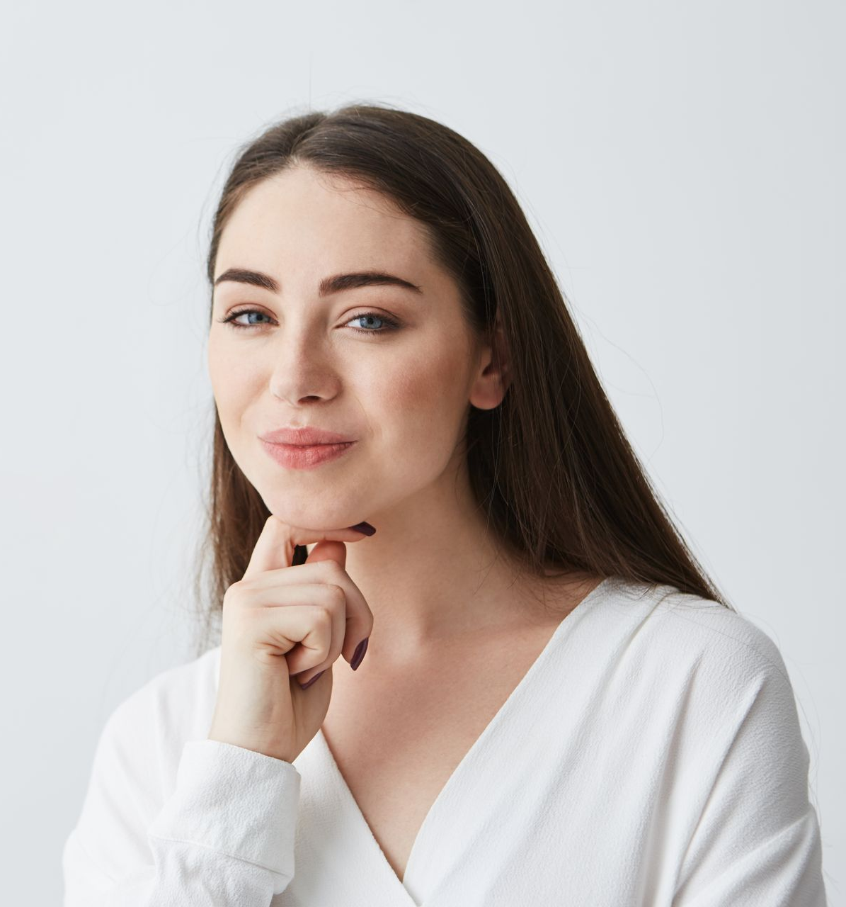 Portrait of a person in a white shirt, resting chin on hand with a slight smile against a light background