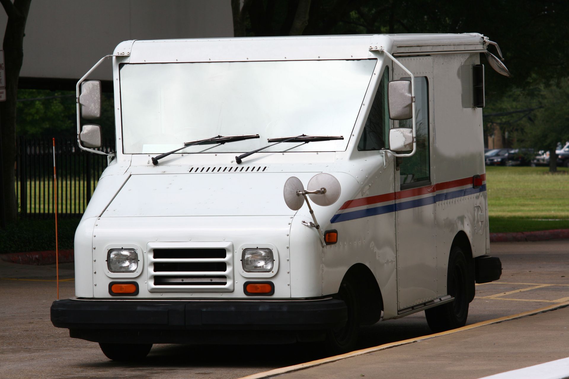 White USPS mail truck on road with red and blue stripes.