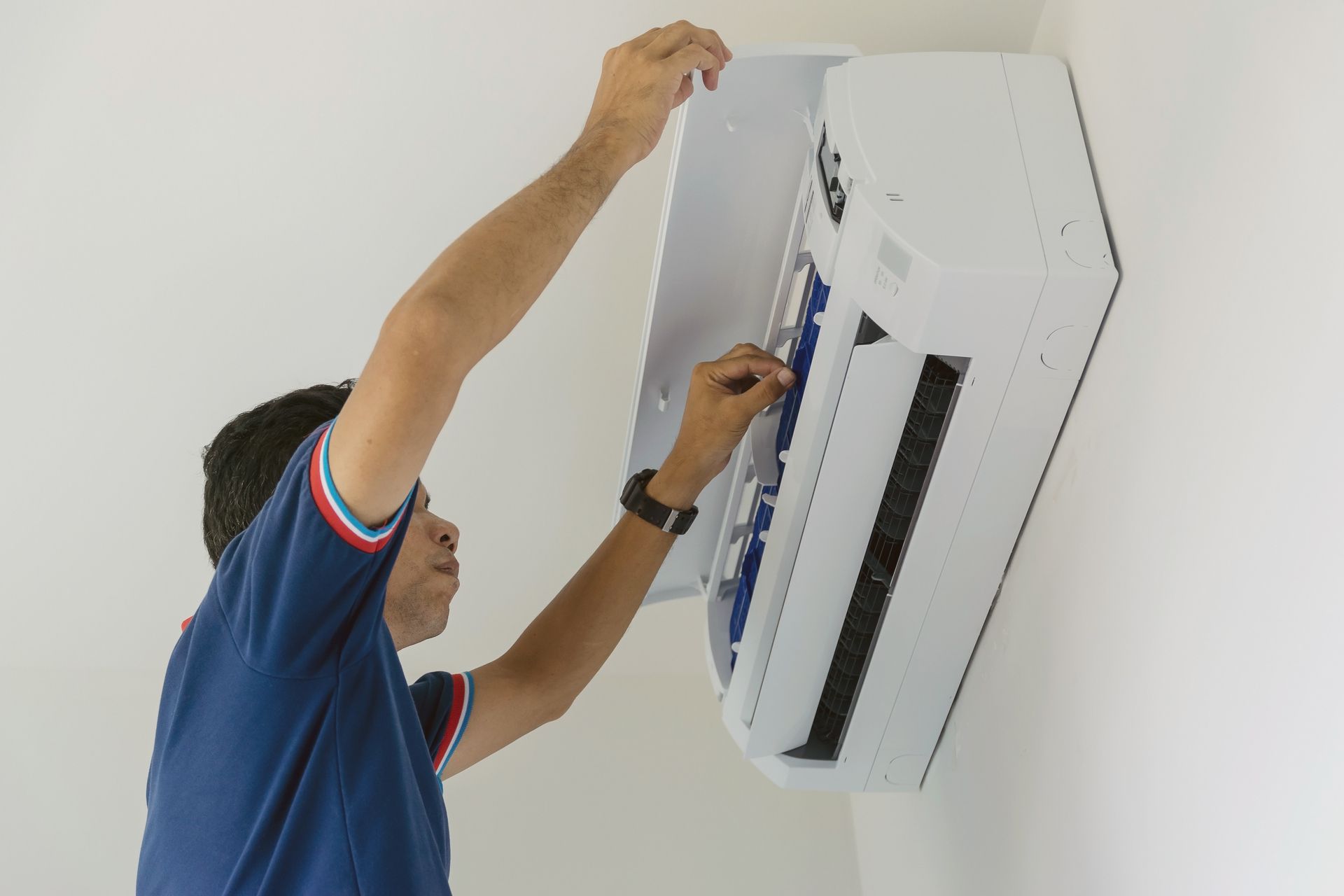 Technician servicing a wall-mounted air conditioner with tools on a white wall