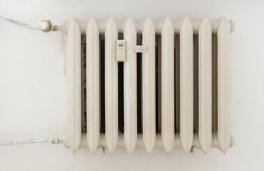 White radiator with a temperature control valve and pipes against a plain wall