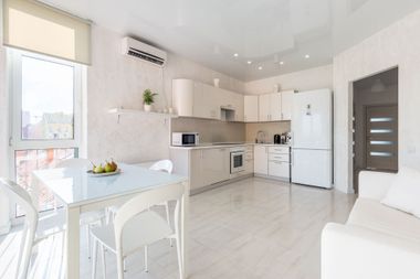 Bright modern kitchen and dining area with white cabinets, table, sofa, and large window