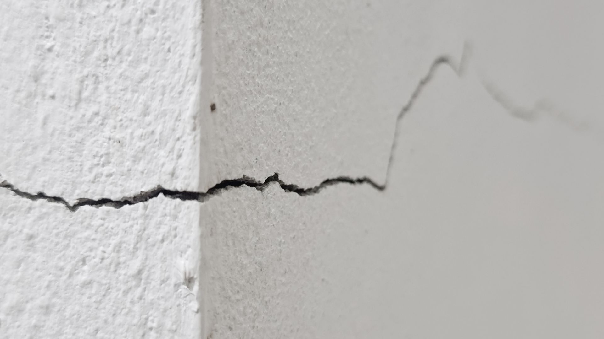 Horizontal crack in a white painted wall with a jagged vertical section near the center.