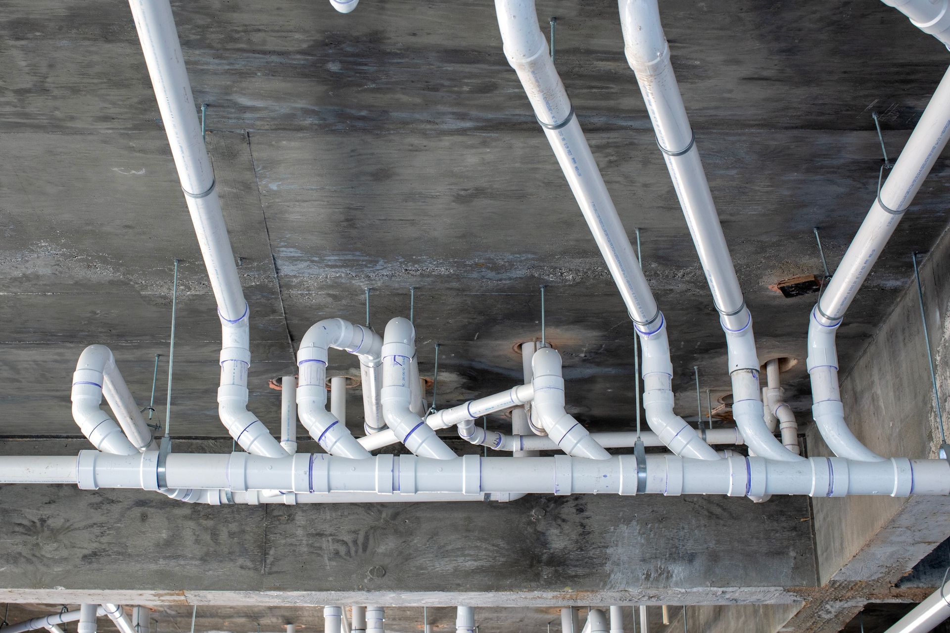 White insulated pipes run along a concrete ceiling in an industrial utility space.