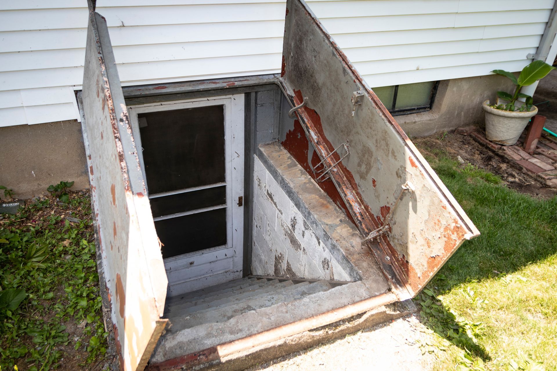 Basement stairwell with open hatch doors leading down to a dark entrance outside a house.