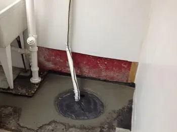 Open manhole with pipes and a gray control box in a concrete utility pit