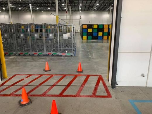 Warehouse aisle with orange cones, red floor markings, and stacked carts near a storage area