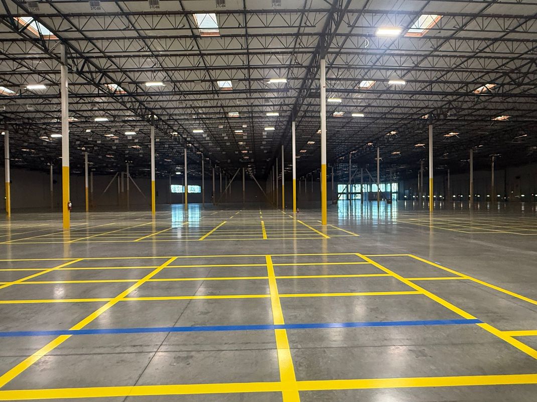Empty warehouse interior with yellow floor grid lines and high industrial ceiling lights