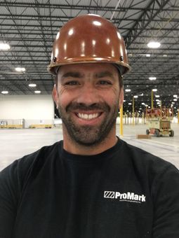 Four men smiling in a warehouse, taking a selfie among yellow safety barriers.
