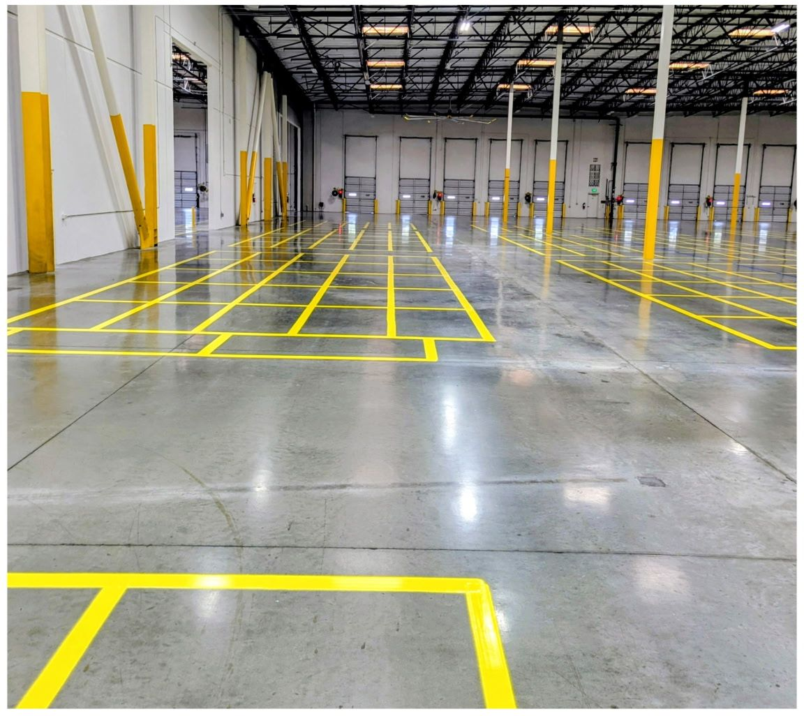 Empty warehouse with yellow floor markings and concrete pillars under a high ceiling