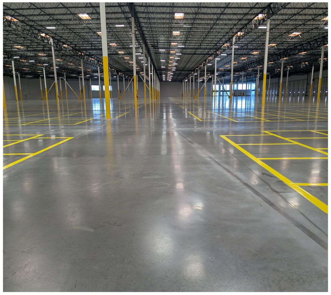 Empty warehouse interior with polished concrete floor and yellow safety markings on support columns and lanes