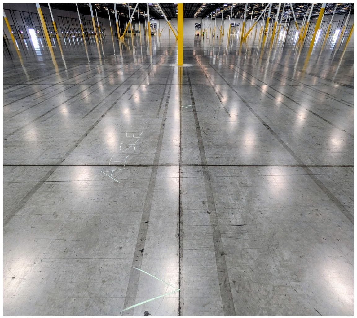 Empty warehouse floor with glossy concrete and rows of yellow posts reflected in the surface