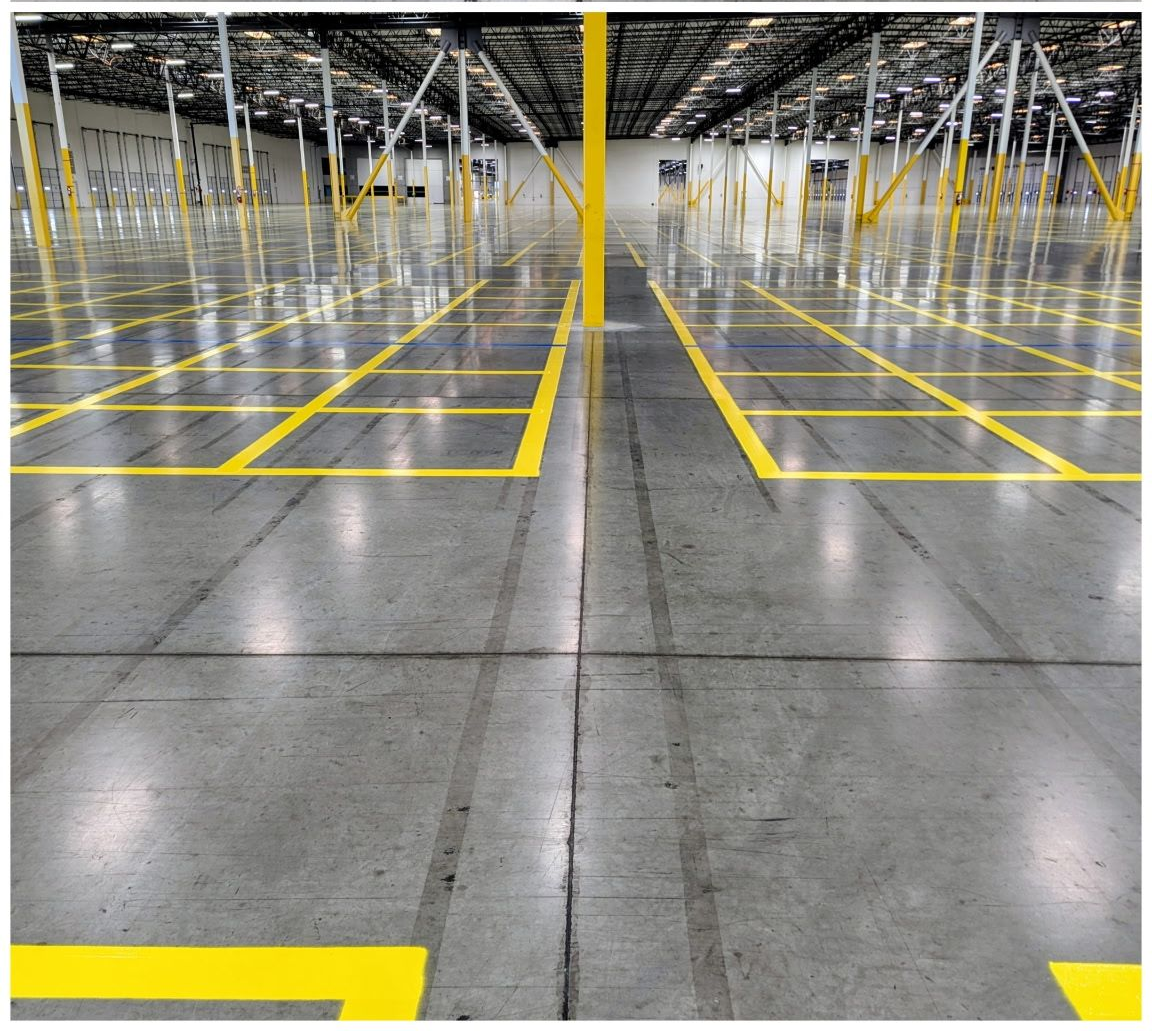 Empty warehouse with glossy concrete floor and yellow aisle markings under overhead lights