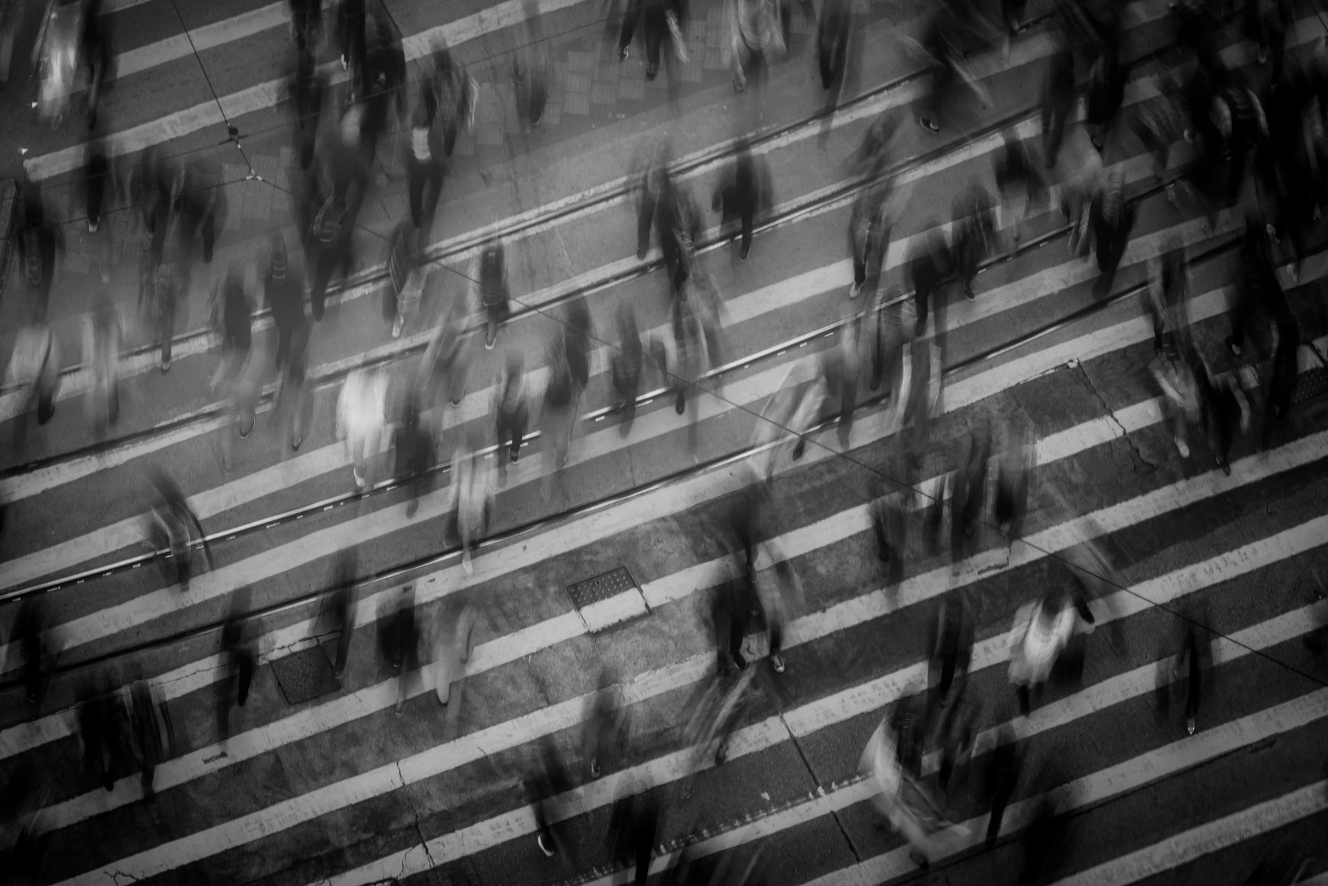 A black and white photo of a crowd of people crossing a street.