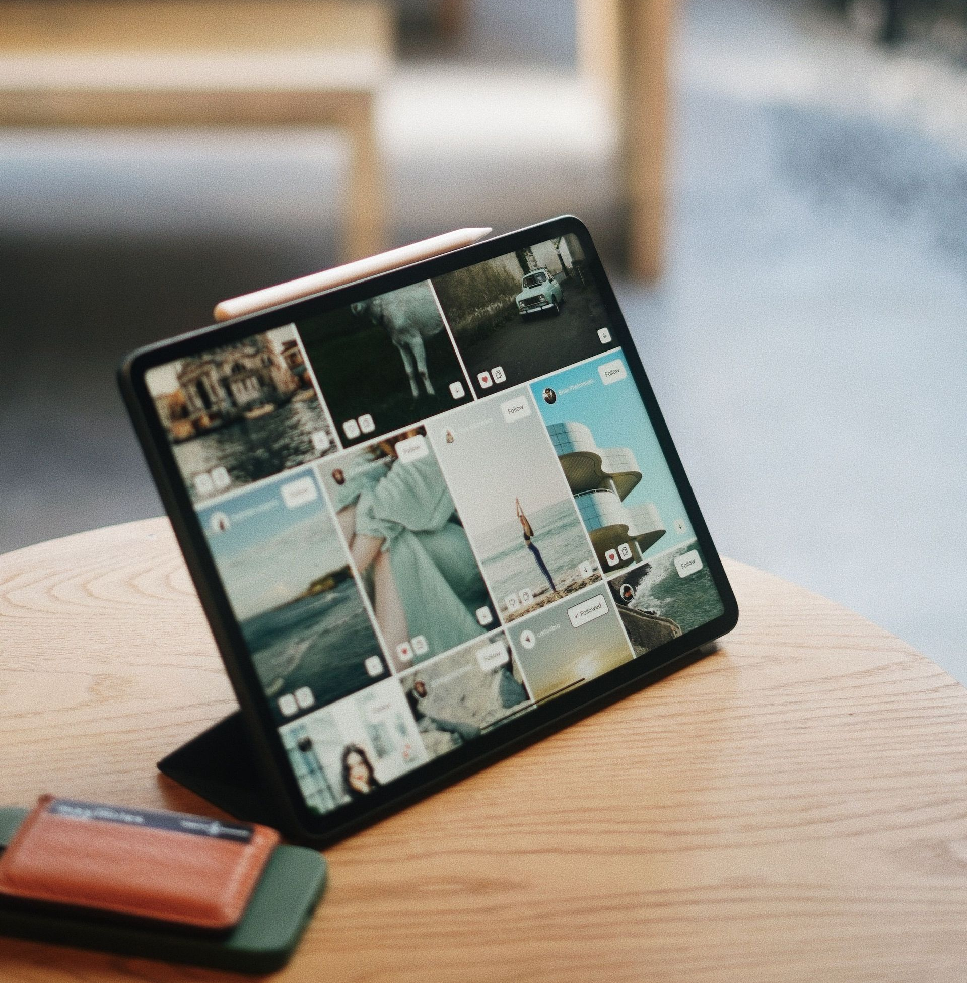Tablet on a wooden table displaying a photo grid, with a wallet beside it.