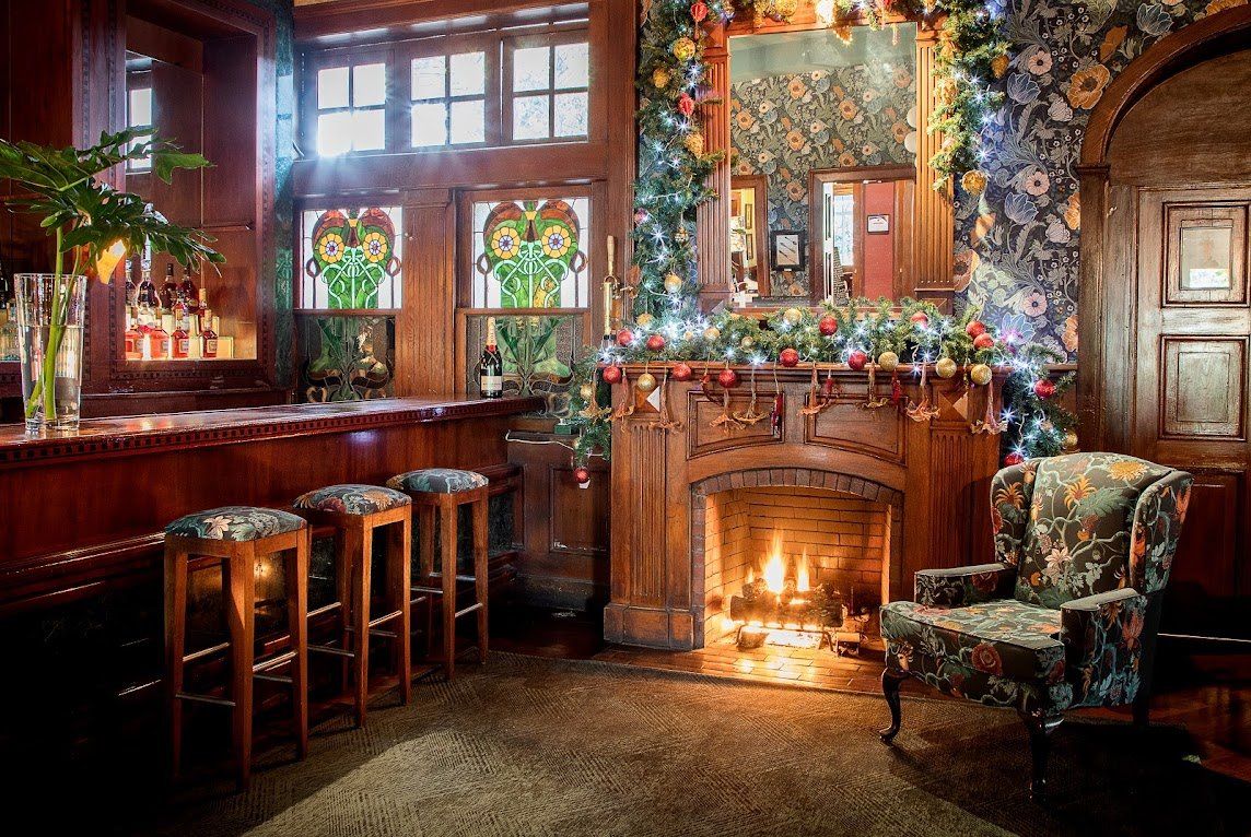 Interior acogedor de pub con chimenea encendida, taburetes de madera en la barra, vidrieras y decoración festiva navideña.