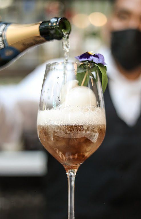 Champán servido en una copa flauta adornada con flores moradas en un bar.