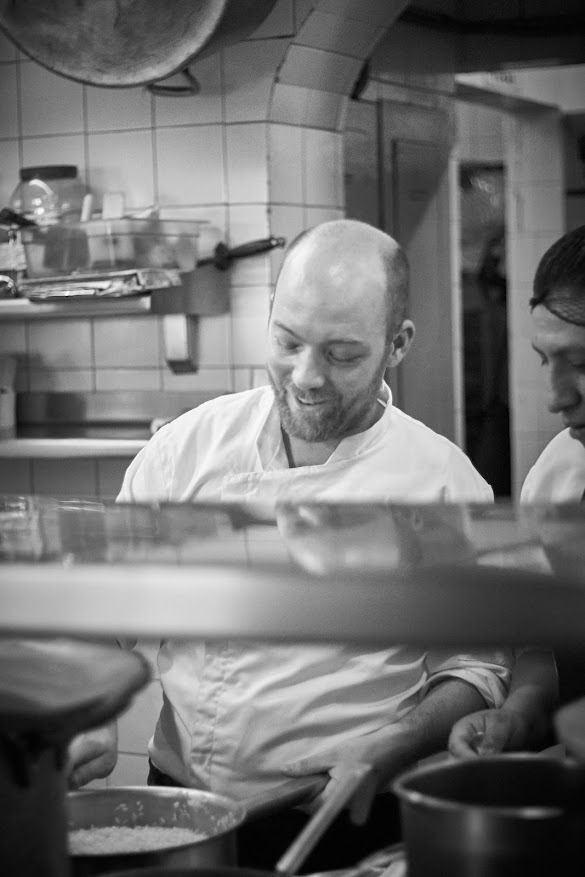 Chef emplatando comida en una cocina, mirando hacia abajo con expresión concentrada.