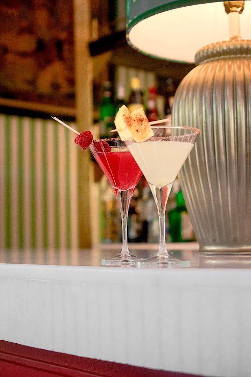 Dos coloridos cócteles sobre la barra de un bar junto a una lámpara.