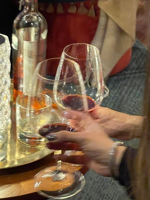 Dos personas chocan sus copas de vino junto a una botella sobre una mesa en un acogedor ambiente interior.