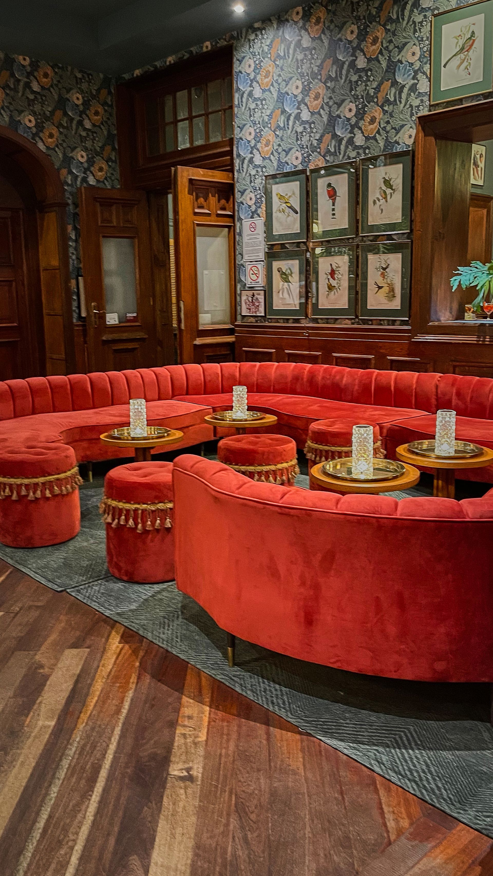 Sofás de terciopelo rojo en un bar de estilo vintage con poca luz, papel pintado estampado y suelos de madera.