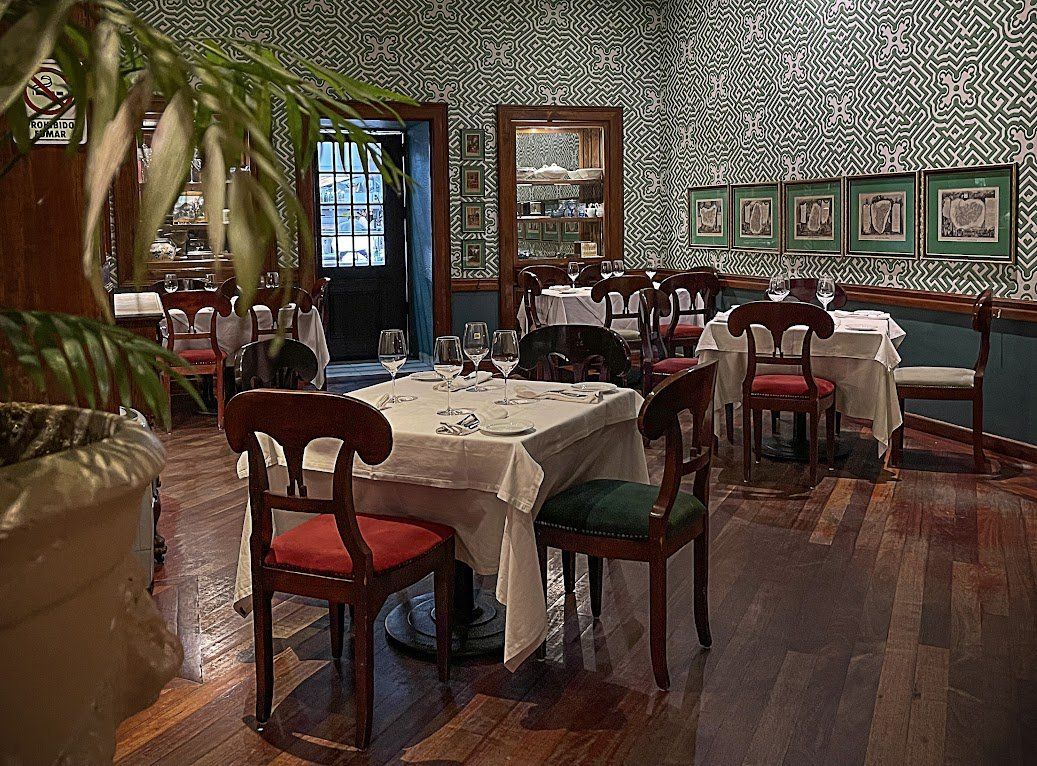 Elegante comedor de restaurante con manteles blancos, sillas rojas, cuadros enmarcados en las paredes y suelos de madera.