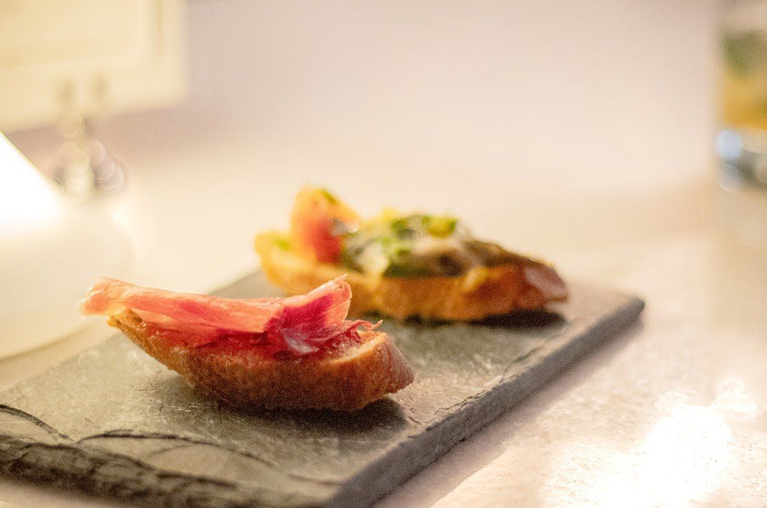 Dos pequeños aperitivos sobre una losa de piedra, uno cubierto con pescado rosado y el otro con una guarnición colorida.