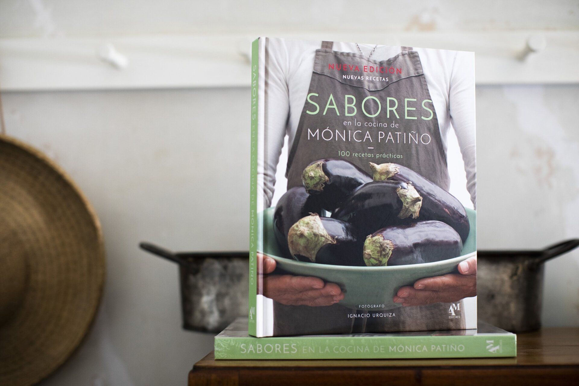 Un libro de cocina titulado “Sabores” sobre una mesa con cuencos y un sombrero al fondo.