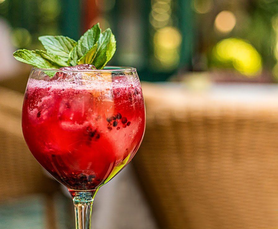 Cóctel de frutos rojos con guarnición de menta en una copa de tallo sobre una mesa, fondo exterior borroso.