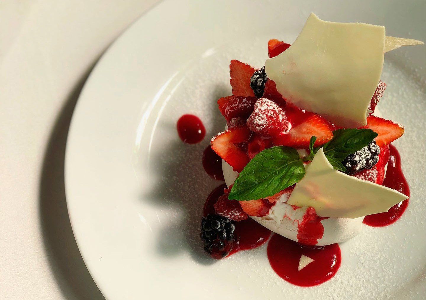 Plato de postre con fresas, frutos rojos, menta y virutas de chocolate blanco sobre un plato blanco.