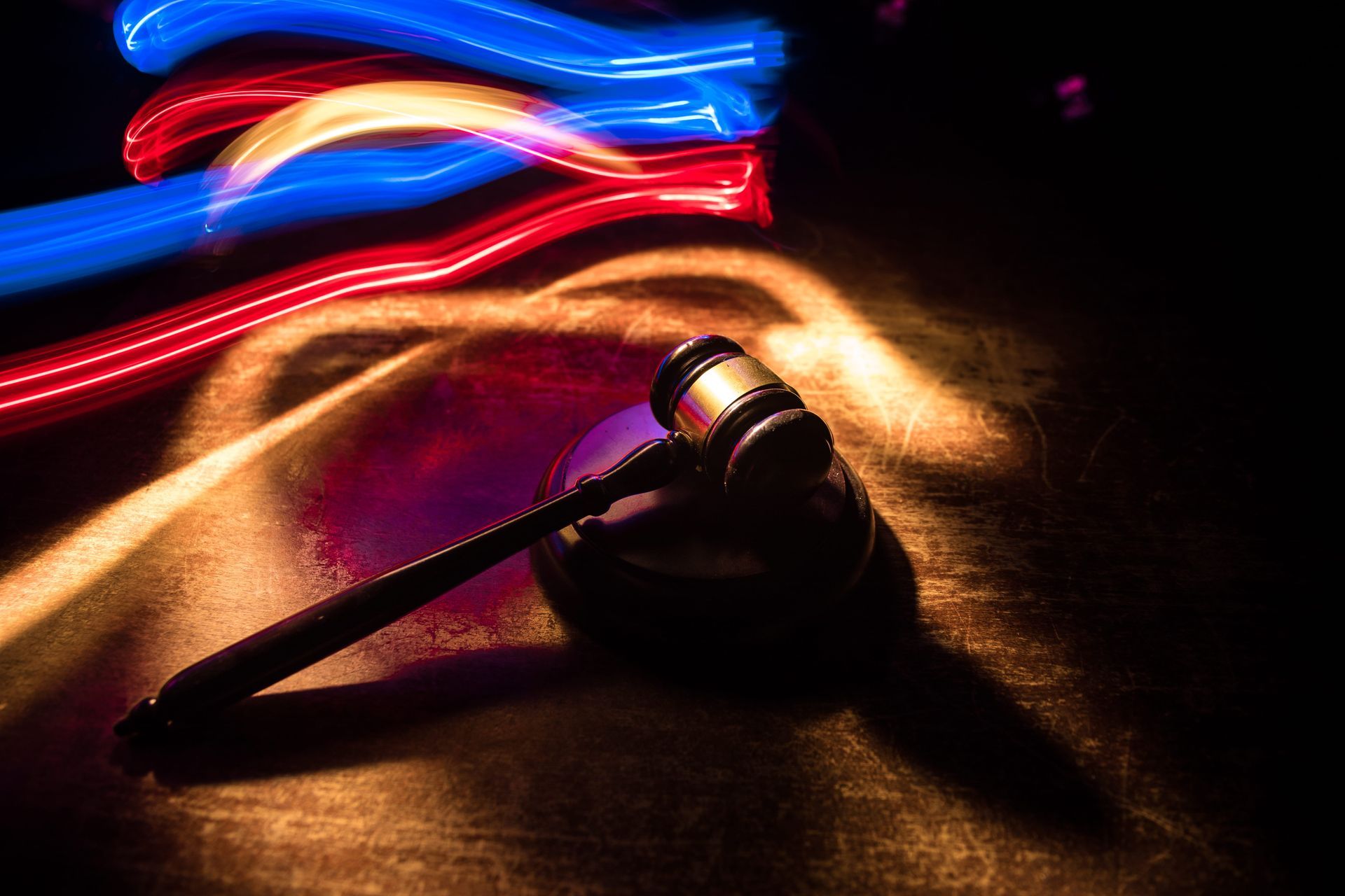 A wooden gavel rests on a round base, illuminated by streaks of red and blue light against a dark background.