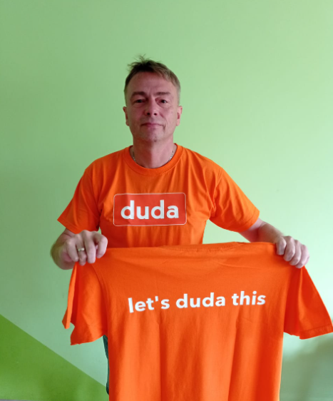 A man is holding an orange shirt that says duda let 's duda this