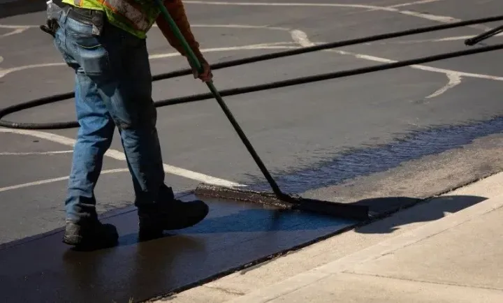 Worker applying sealcoat to an asphalt parking lot.