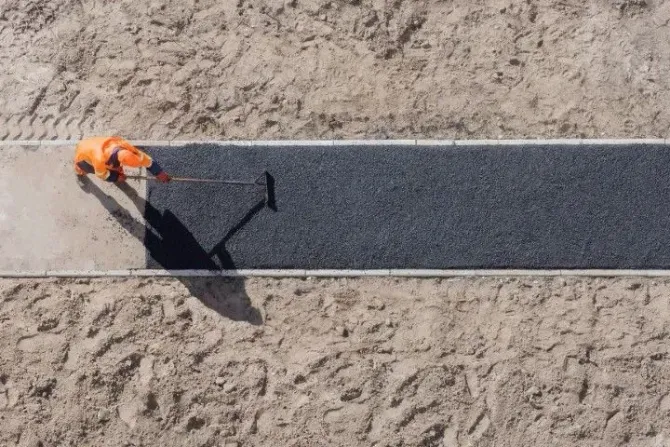 Worker spreading asphalt on a new sidewalk.