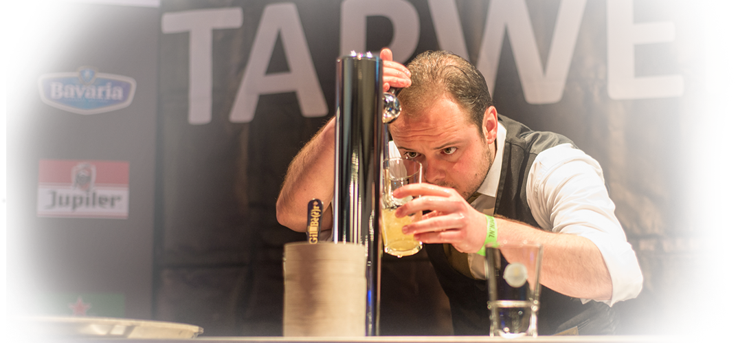 Man leunt over een biertap en proeft een schuimend drankje. Hij bevindt zich in een wedstrijdsetting.