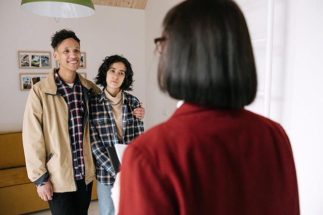 young-couple-speaking-with-a-woman-holding-a-clipboard-inside-a-home
