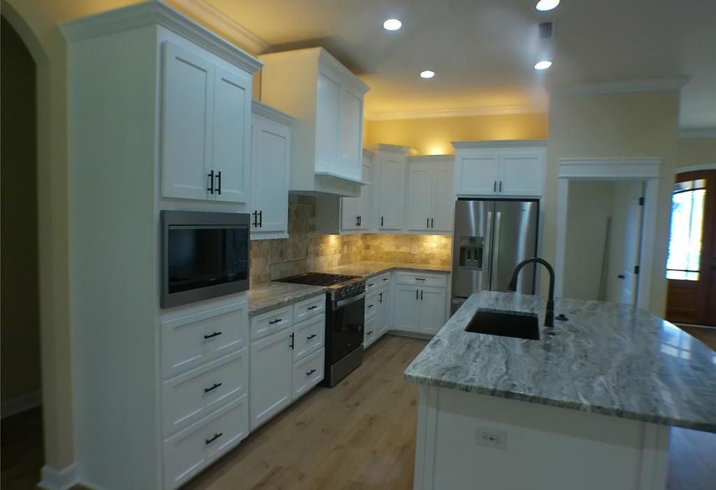 White kitchen with granite countertops, stainless steel appliances, and an island.
