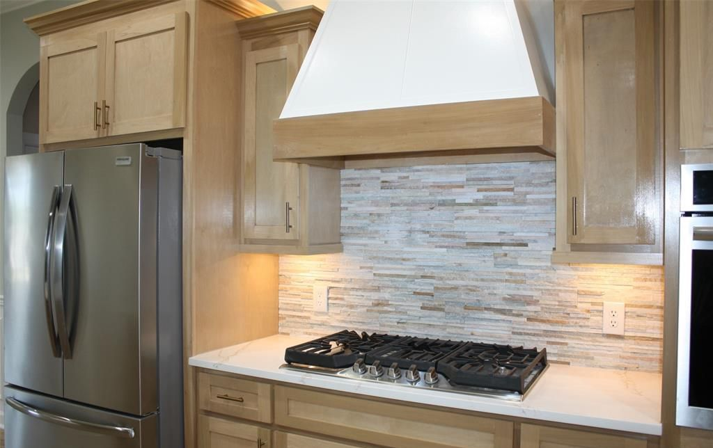 Kitchen with light wood cabinets, stainless steel appliances, and stone backsplash.