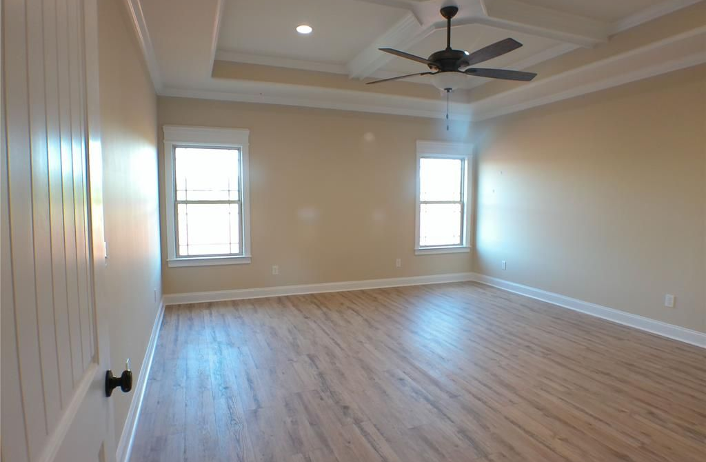 Empty beige bedroom with hardwood floors, two windows, and a ceiling fan.