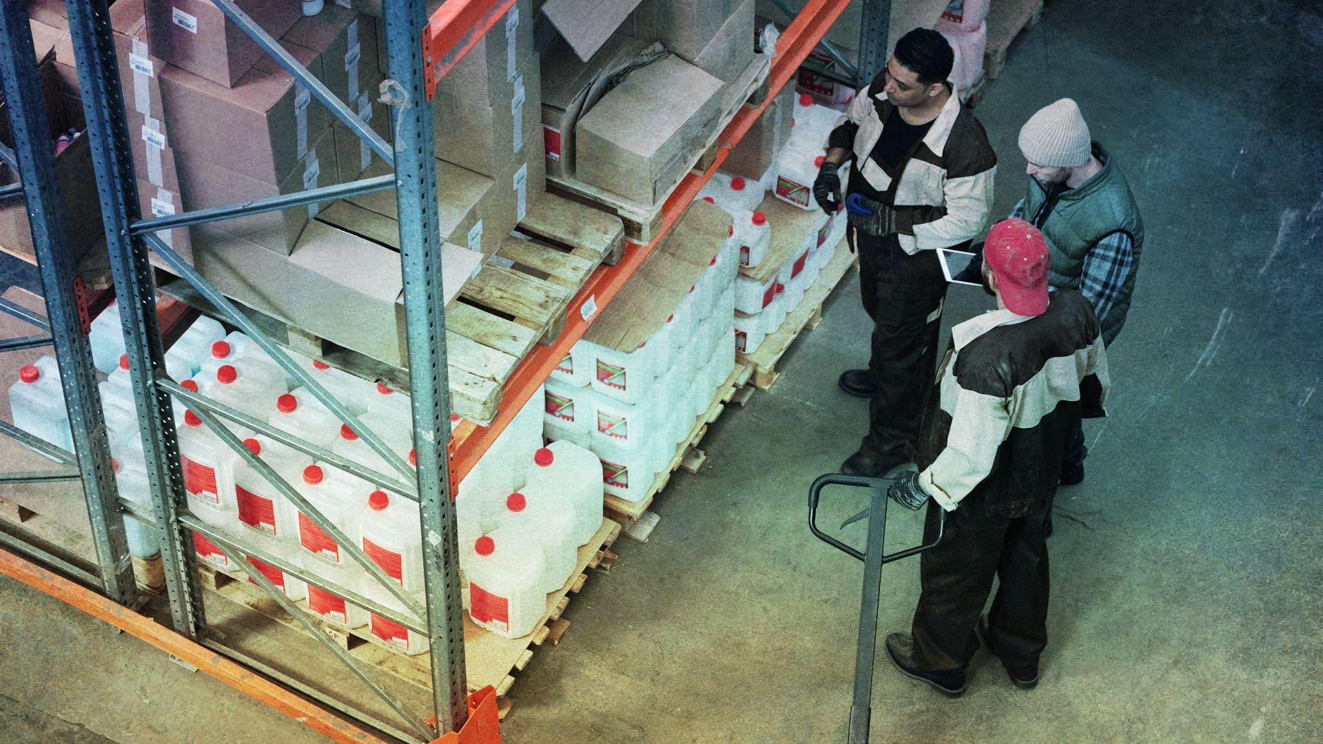 A group of people are standing around a pallet truck in a warehouse.