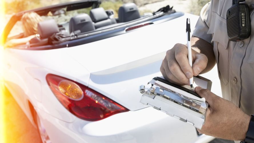 a police officer writes a ticket in front of a white car