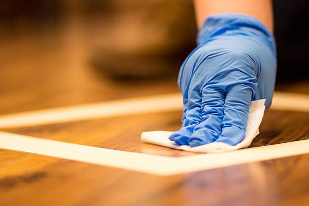 Blue-gloved hand wiping a wooden surface with a white cloth