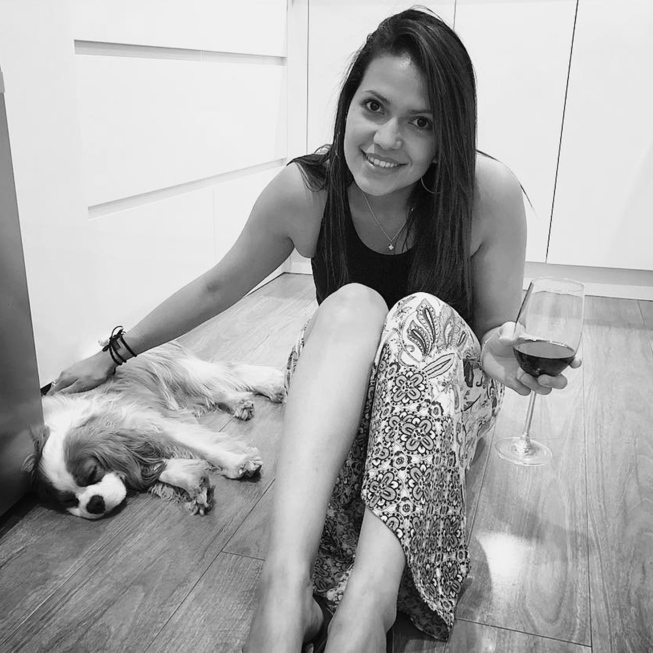 Ale Amaya sitting on a wooden floor beside a relaxed dog, smiling at the camera.